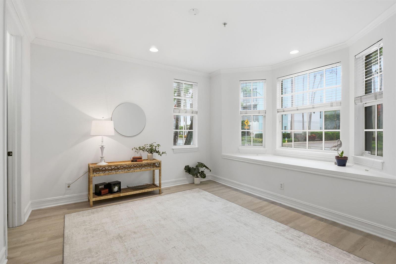 A bright, empty room features light wood flooring, a bay window, and a console table — 349 E Mallory Circle, Delray Beach FL 33483, DELRAY BEACH, FL