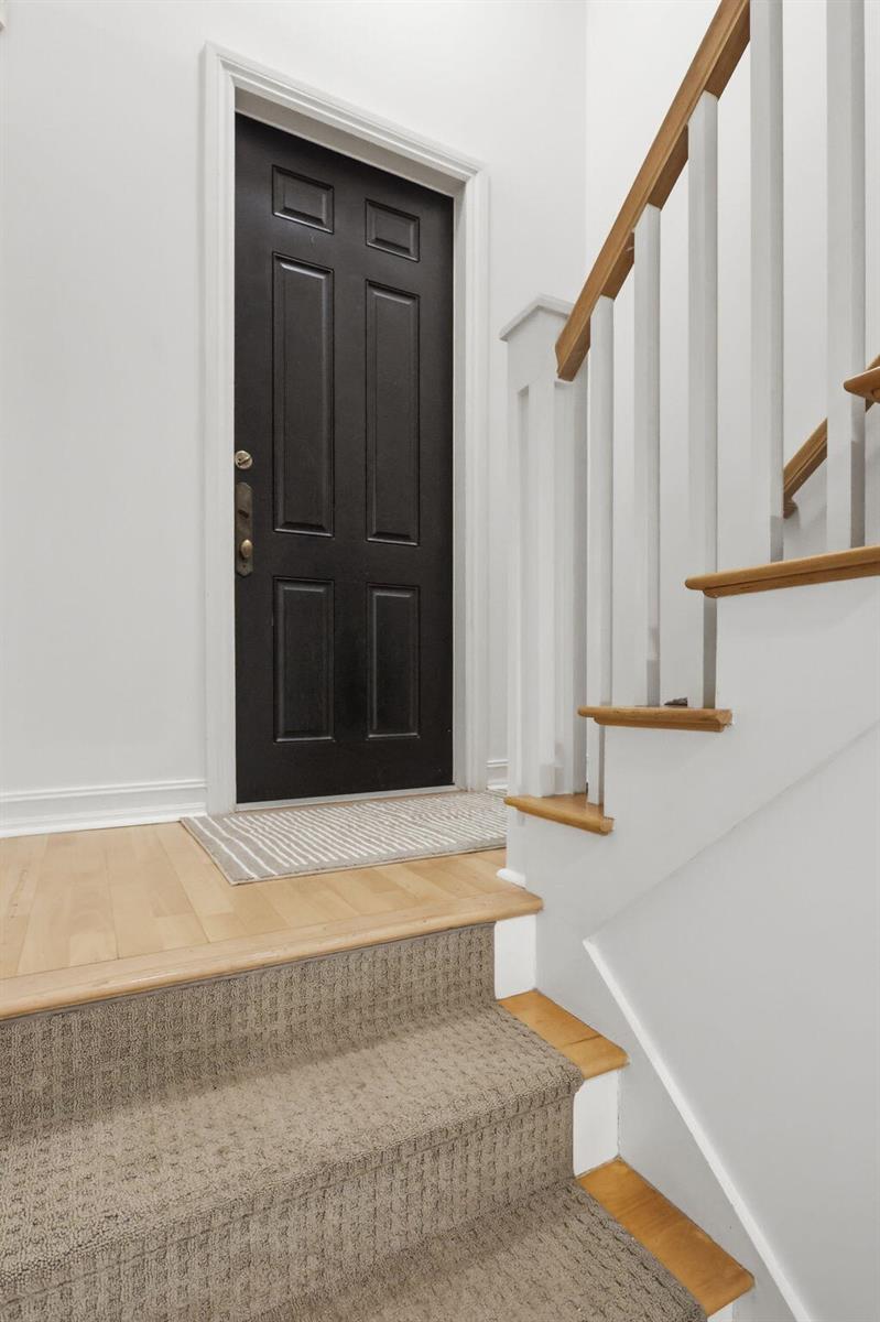 A black front door sits next to a staircase with carpeted treads and wooden railings — 349 E Mallory Circle, Delray Beach FL 33483, DELRAY BEACH, FL
