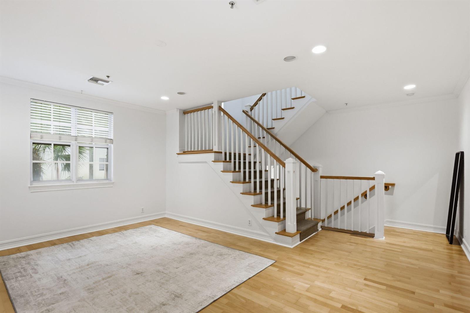 A bright room with hardwood floors, a large area rug, and a central wooden staircase — 349 E Mallory Circle, Delray Beach FL 33483, DELRAY BEACH, FL