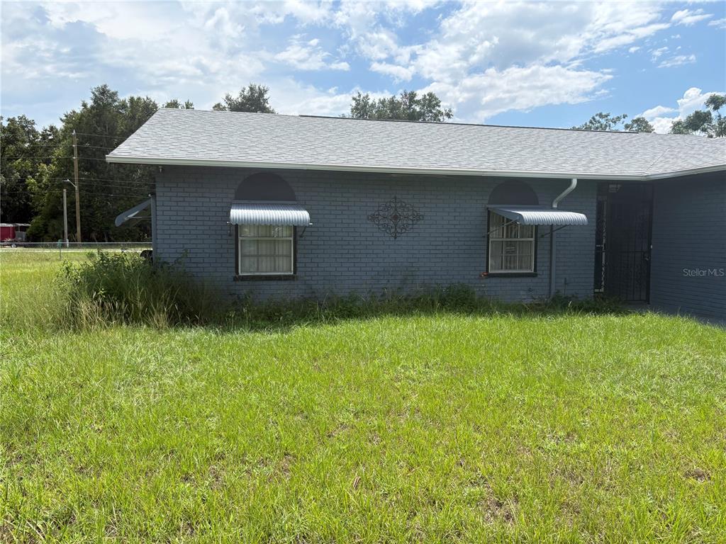 A gray brick house exterior features two windows with metal awnings and a metal door — 10 BAHIA WAY, OCALA, FL