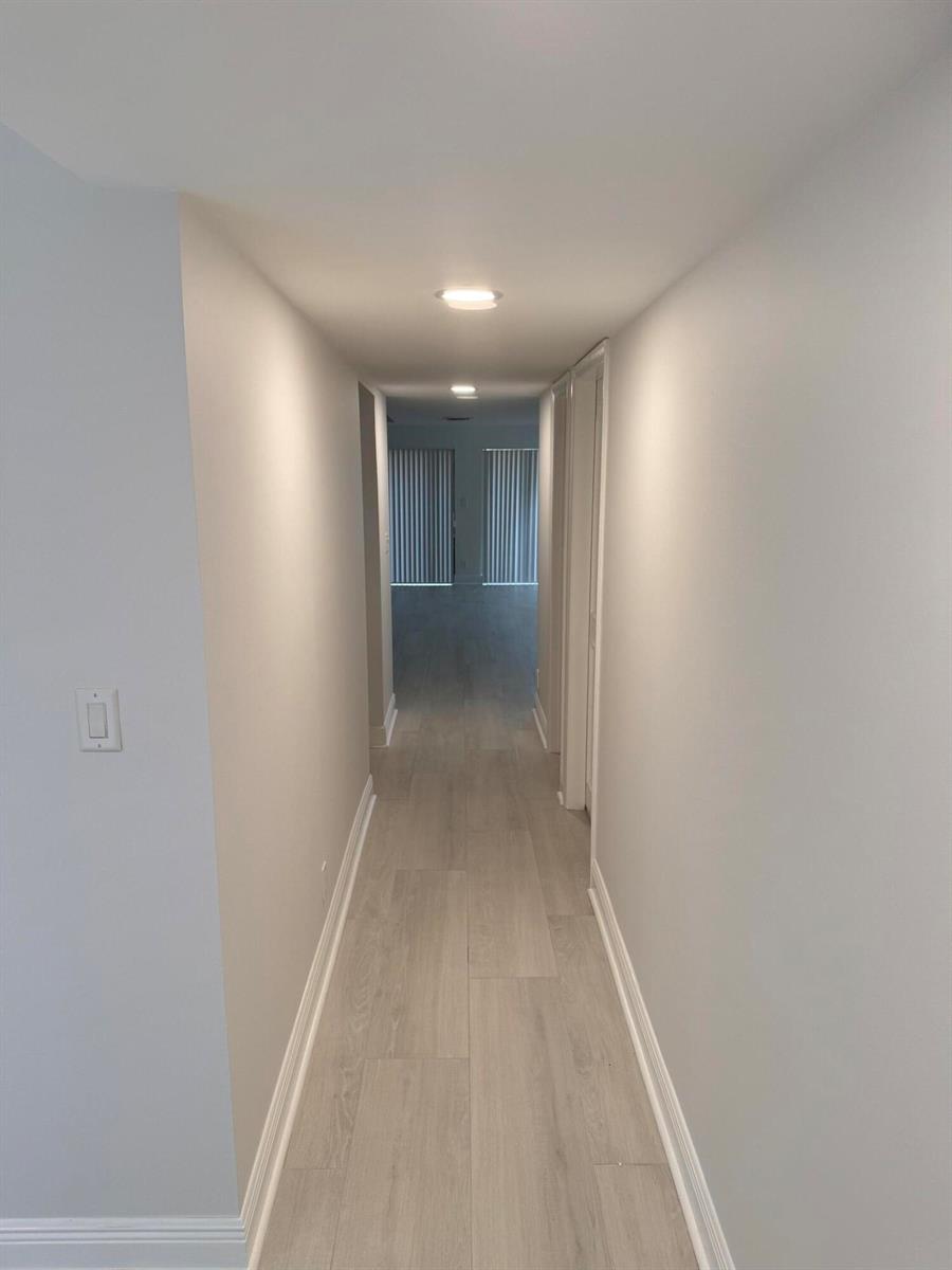 A long, narrow hallway features light-colored wood-look flooring, white walls, and recessed ceiling lighting — 5644 Santiago Circle, Boca Raton FL 33433, BOCA RATON, FL