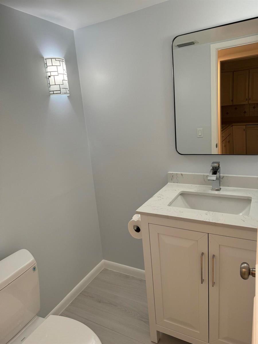A small bathroom features a white vanity with a stone countertop, a mirror, and a sconce — 5644 Santiago Circle, Boca Raton FL 33433, BOCA RATON, FL