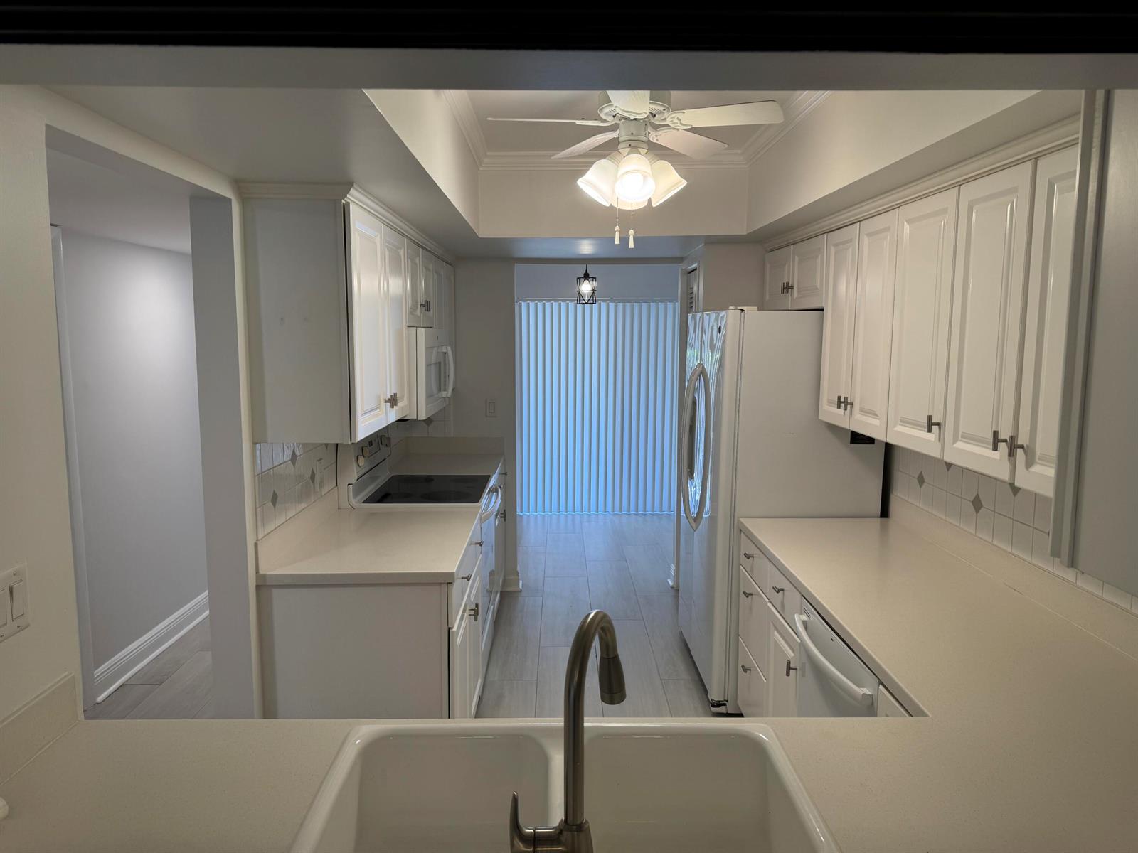 A galley kitchen features white cabinets, light countertops, a double sink, and a ceiling fan — 5644 Santiago Circle, Boca Raton FL 33433, BOCA RATON, FL