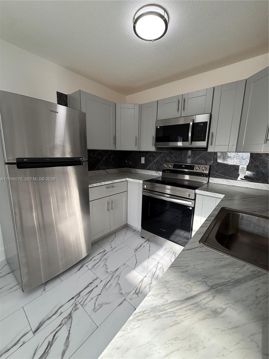 A kitchen features stainless steel appliances, grey cabinetry, and white marble-patterned tile flooring — 6071 SW 33rd St # 4, Miramar FL 33023, MIRAMAR, FL
