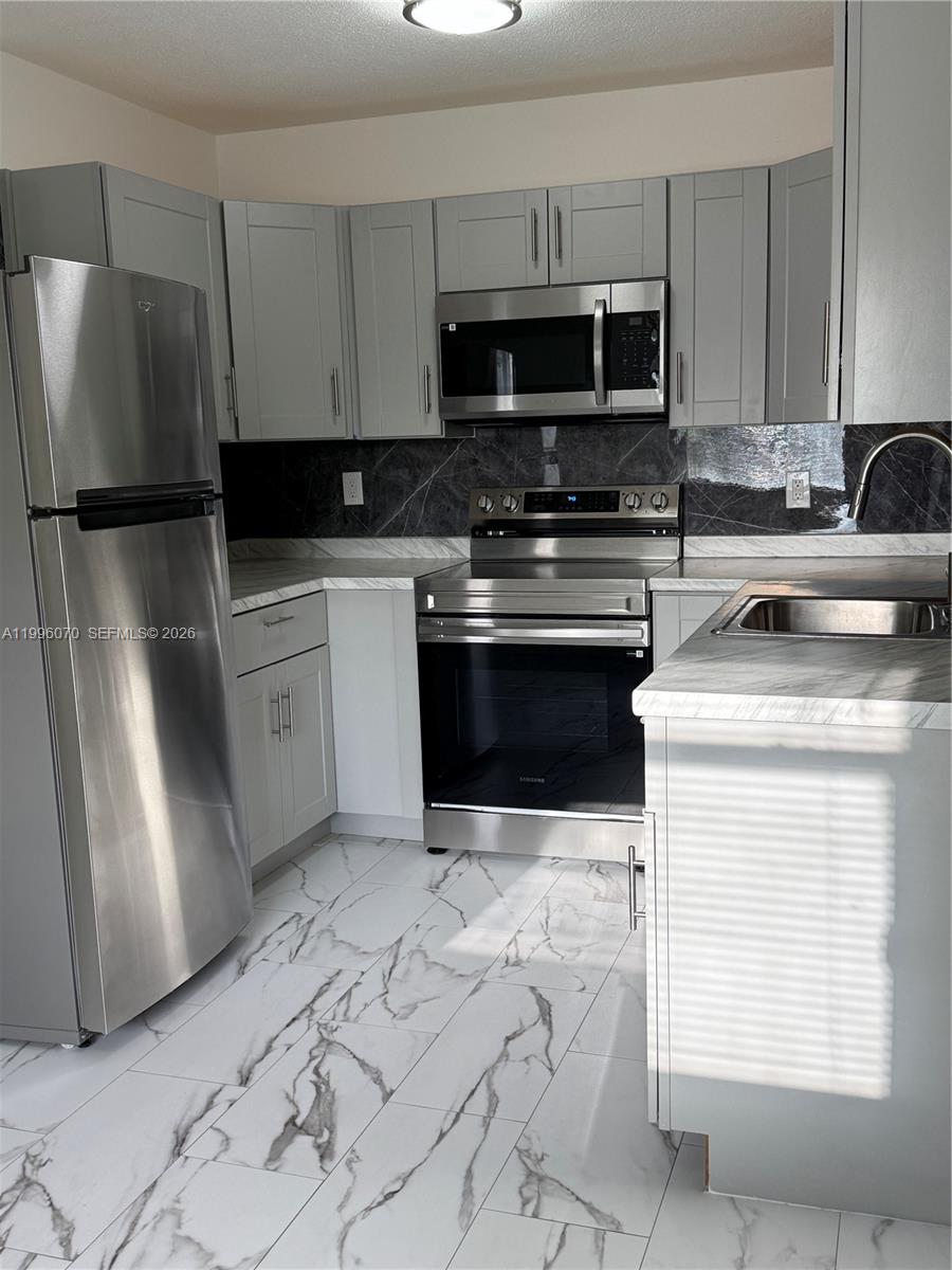 A kitchen features light gray cabinets, stainless steel appliances, and white marble-patterned tile flooring — 6071 SW 33rd St # 4, Miramar FL 33023, MIRAMAR, FL