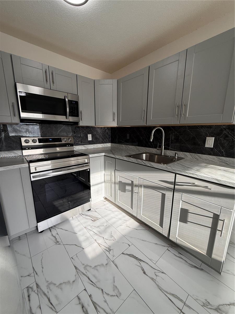 A kitchen features gray cabinets, stainless steel appliances, a black backsplash, and marble-patterned flooring — 6071 SW 33rd St # 4, Miramar FL 33023, MIRAMAR, FL