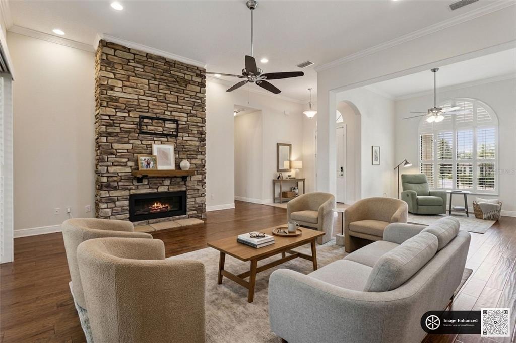 A living room features a stone fireplace, hardwood floors, a ceiling fan, and neutral furniture — 39513 HILLRISE LANE, LADY LAKE, FL