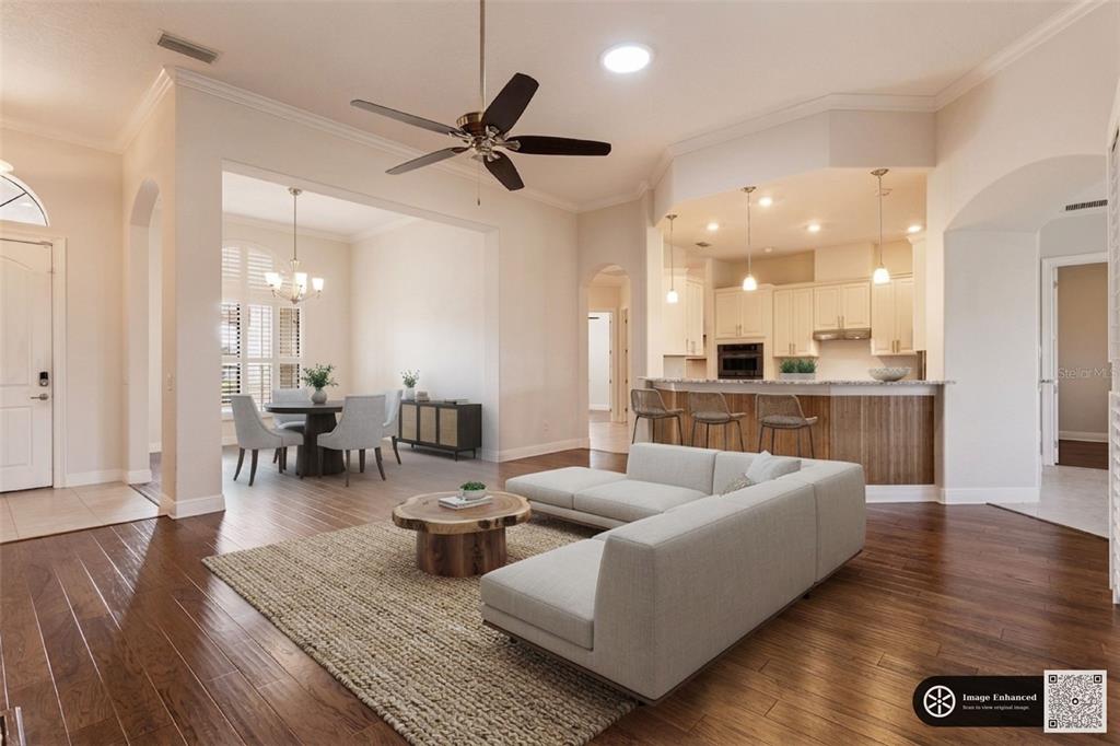 An open-concept living room with hardwood floors, a sectional sofa, and an adjacent kitchen area — 39513 HILLRISE LANE, LADY LAKE, FL
