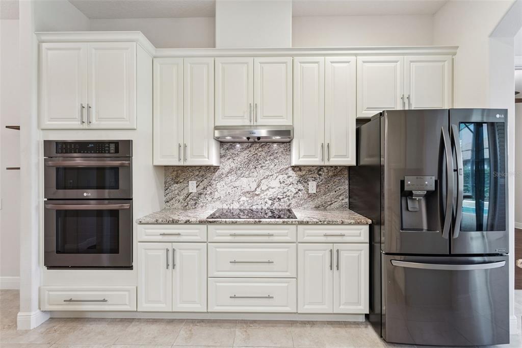 A kitchen features white cabinets, granite countertops, a stainless steel oven, and a dark refrigerator — 39513 HILLRISE LANE, LADY LAKE, FL