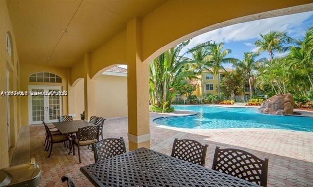 A covered patio with outdoor dining furniture overlooks a swimming pool and palm trees — 5580 NW 61st St # 602, Coconut Creek FL 33073, COCONUT CREEK, FL