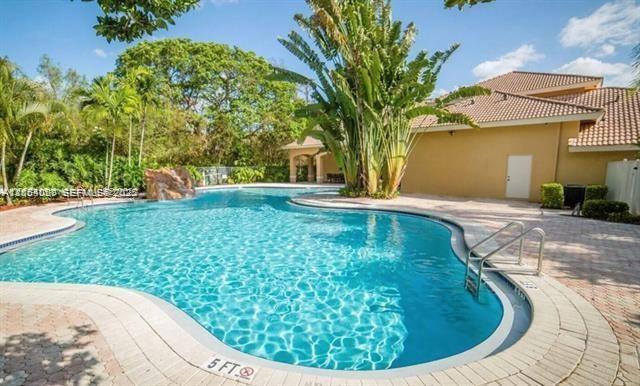A swimming pool with a rock waterfall feature sits beside a tan building with palm trees — 5580 NW 61st St # 602, Coconut Creek FL 33073, COCONUT CREEK, FL