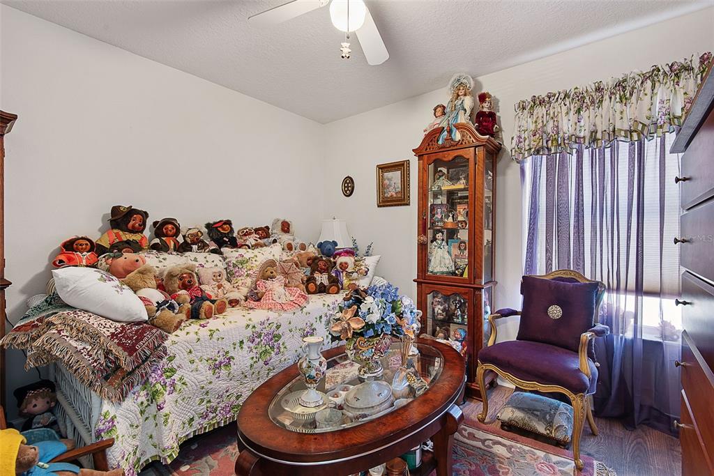 A bedroom features a daybed covered in teddy bears, a glass-topped coffee table, and a curio cabinet — 210 ULLIAN TRAIL, PALM COAST, FL