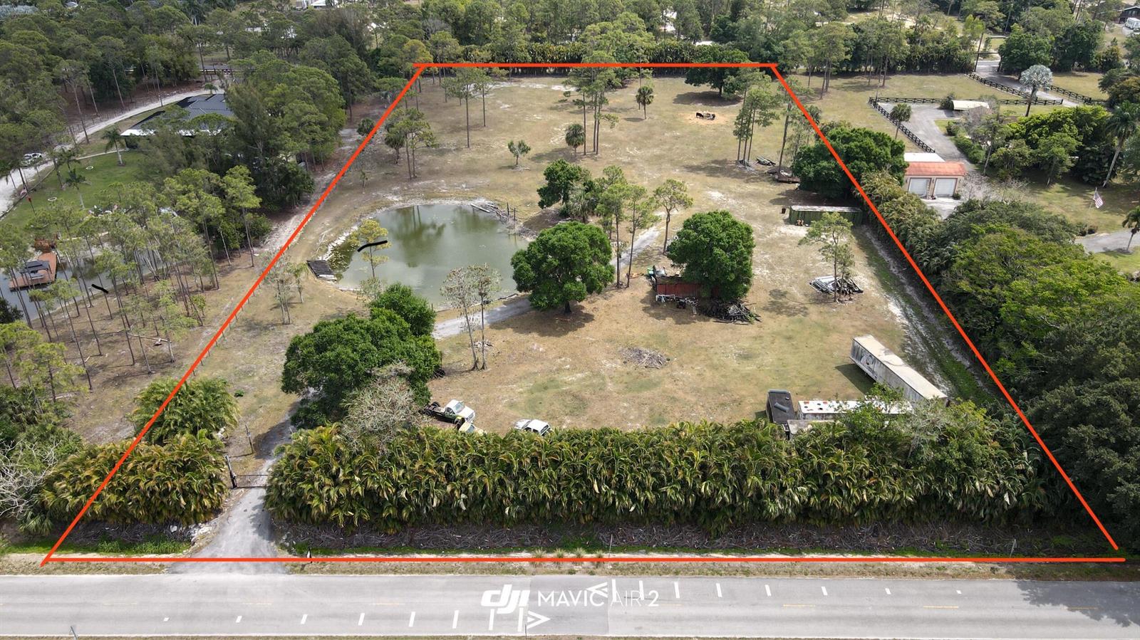 An aerial view shows a large, rectangular grassy lot featuring a pond and scattered trees — 3547 161st Terrace N, FL 33470, FL