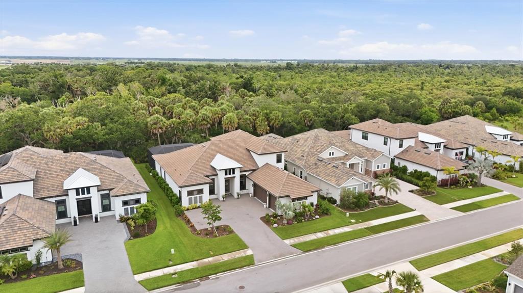 An aerial view shows several suburban houses with tiled roofs and driveways near a forest — 9463 TEQUILA SUNRISE DRIVE, SARASOTA, FL
