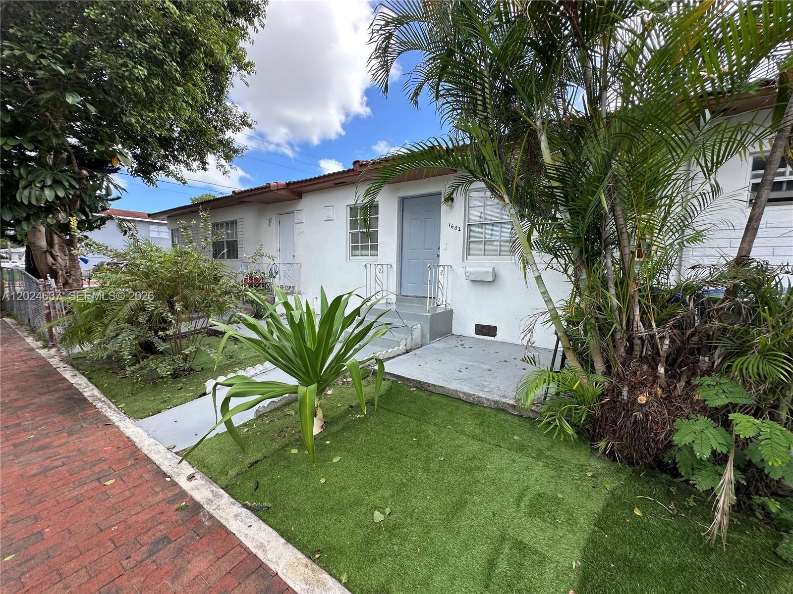 A white single-story duplex features a gray front door, artificial turf, and palm trees — 600 SW 16th Ave, Miami FL 33135, MIAMI, FL