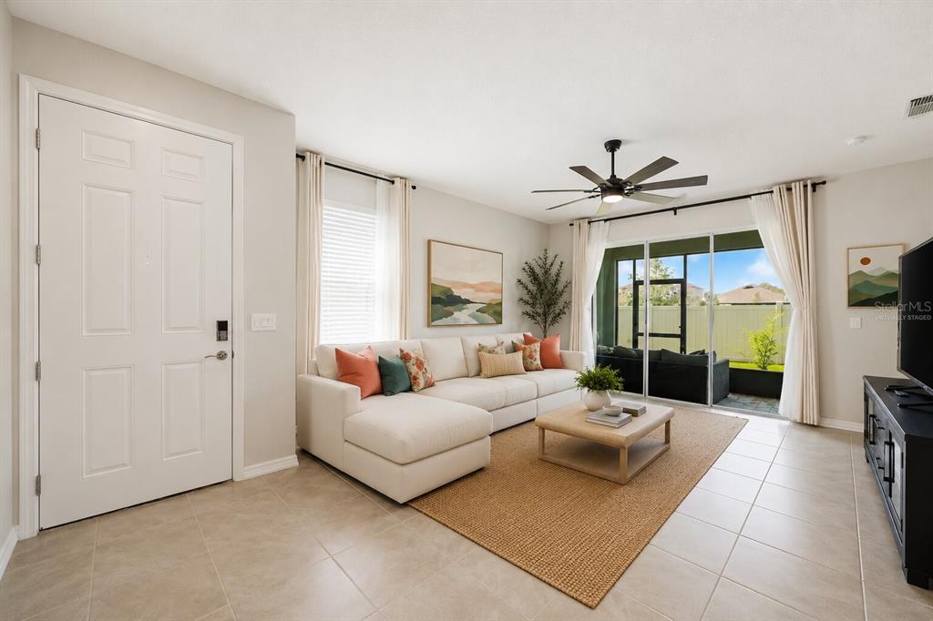 A living room with a white sectional sofa, coffee table, tile floors, and sliding glass doors — 31398 ANCIENT SAGE ROAD, WESLEY CHAPEL, FL