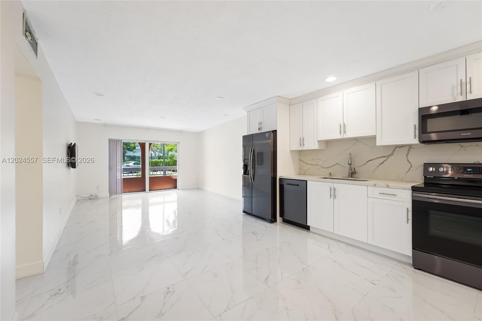 A modern kitchen with white cabinets and marble-style flooring opens into a bright living area — 7920 Camino Real # 109, Miami FL 33143, MIAMI, FL
