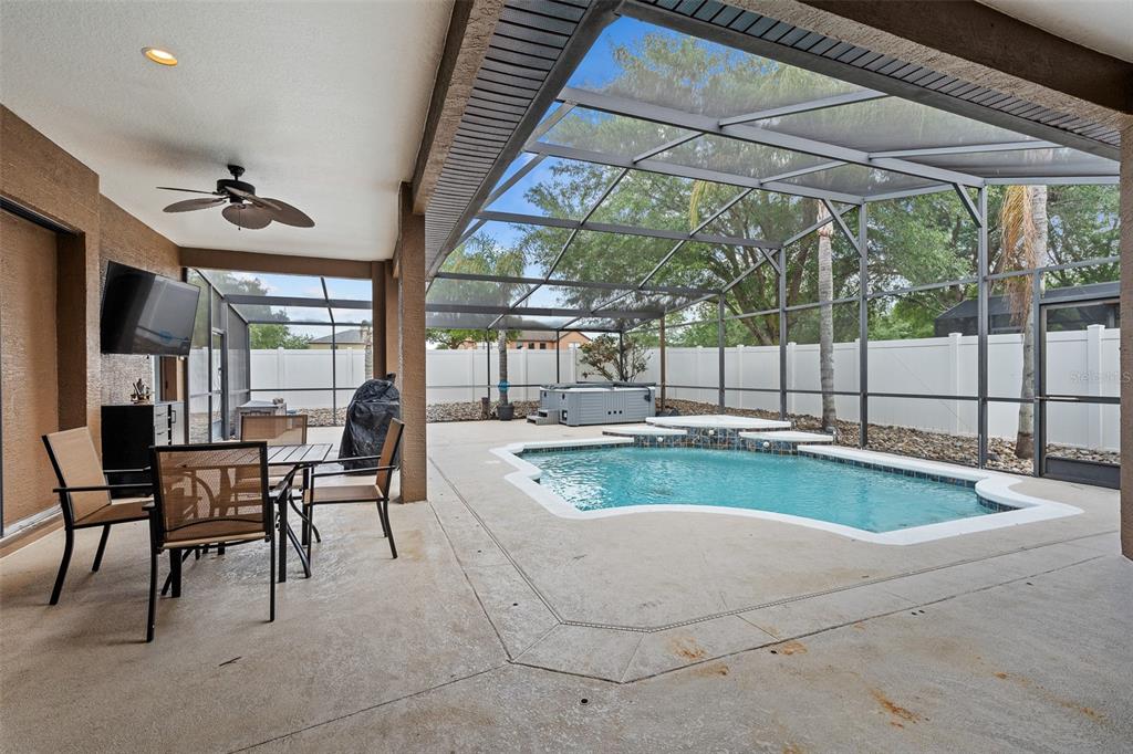 A covered patio features a dining set, a television, and a screened-in pool and spa — 1059 NATURAL OAKS DRIVE, ORANGE CITY, FL