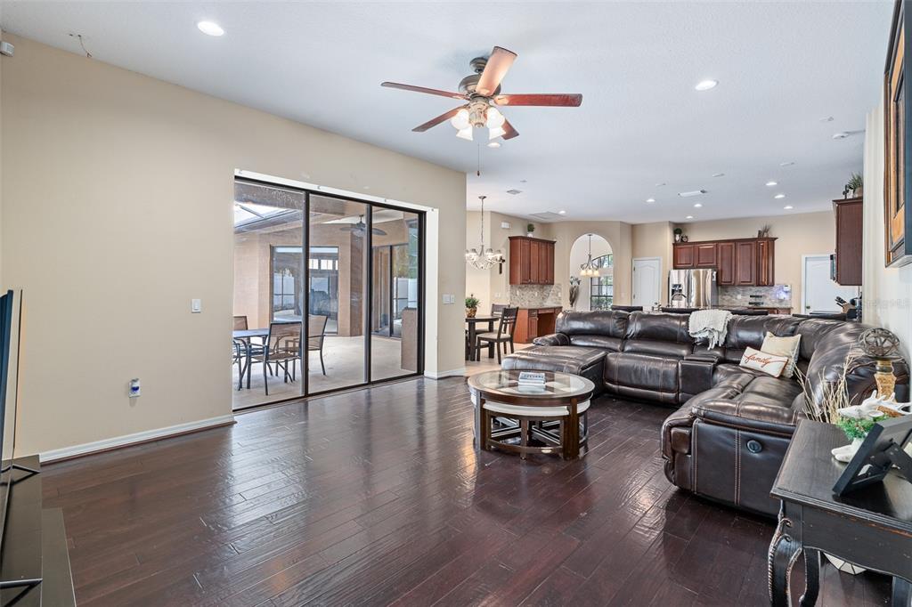 A spacious living room features dark wood floors, a large leather sectional, and sliding glass doors — 1059 NATURAL OAKS DRIVE, ORANGE CITY, FL