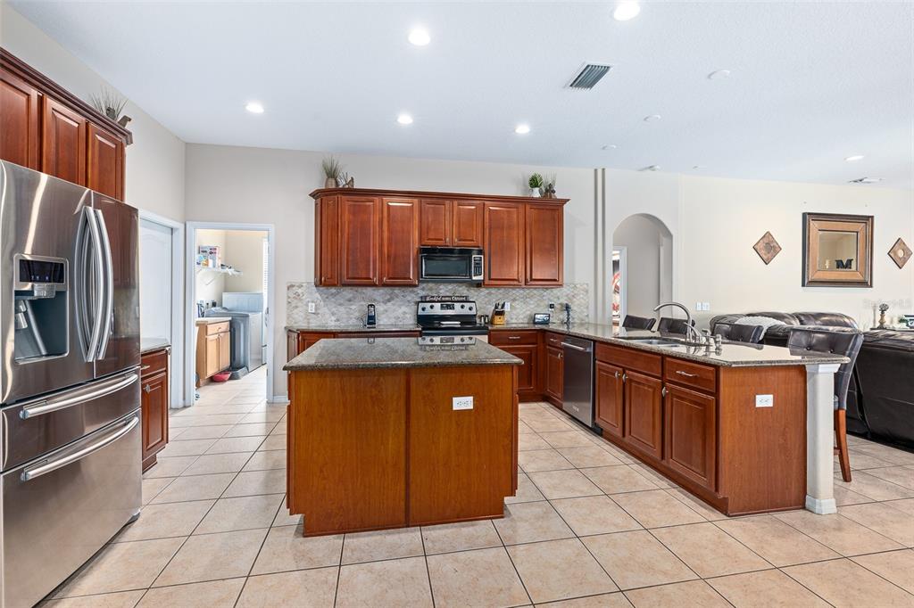 A kitchen features wood cabinets, granite countertops, a central island, and stainless steel appliances — 1059 NATURAL OAKS DRIVE, ORANGE CITY, FL