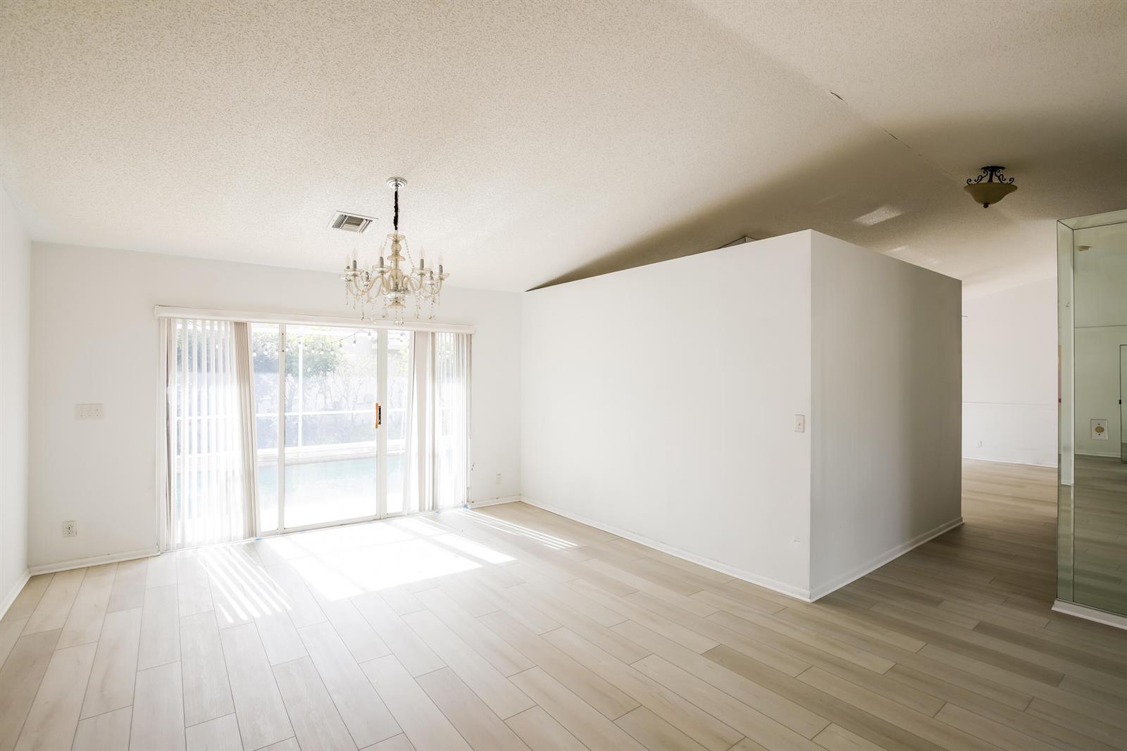 A bright room with light wood-look flooring, a crystal chandelier, and sliding glass patio doors — 5491 NW 40th Terrace, Coconut Creek FL 33073, COCONUT CREEK, FL