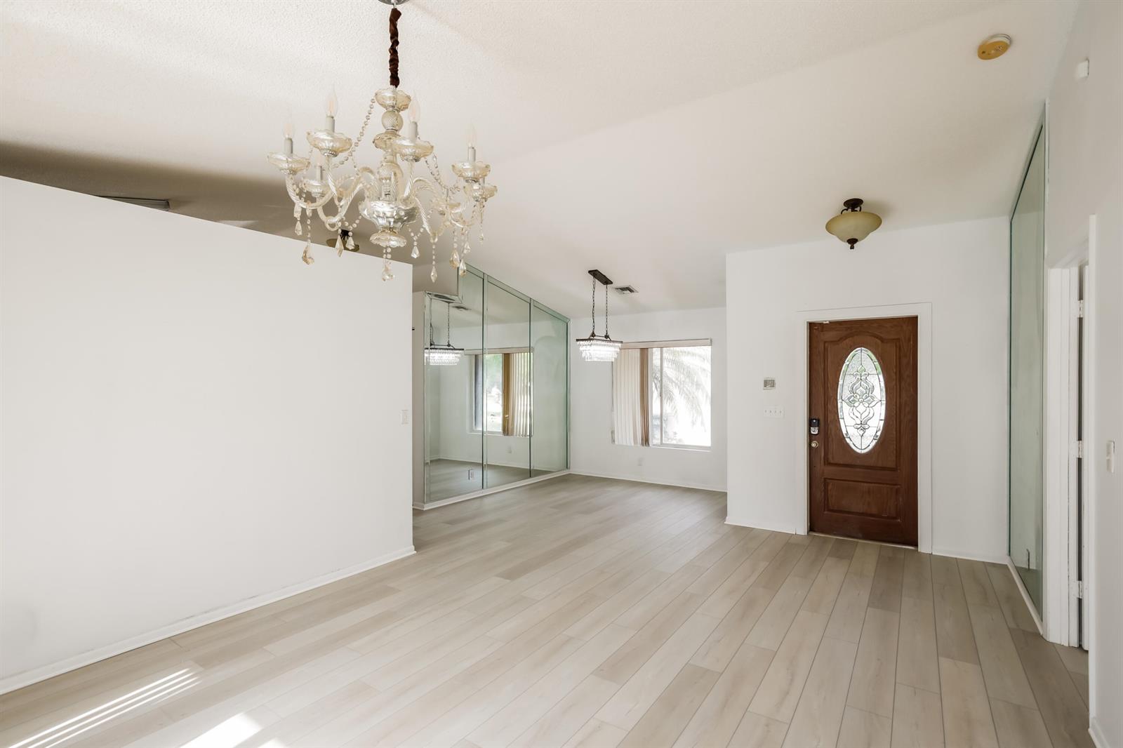 An entryway with light wood flooring, a crystal chandelier, mirrored walls, and a wooden door — 5491 NW 40th Terrace, Coconut Creek FL 33073, COCONUT CREEK, FL