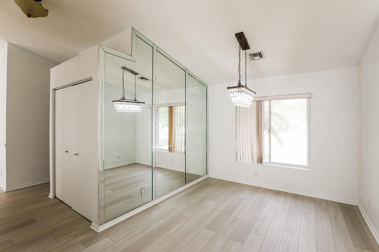 A room with light wood-look flooring, a crystal chandelier, and a large mirrored wall — 5491 NW 40th Terrace, Coconut Creek FL 33073, COCONUT CREEK, FL