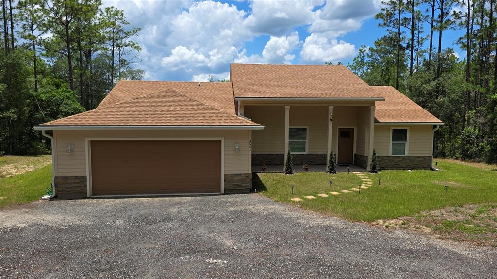 A tan, single-story house with a two-car garage, stone accents, and a gravel driveway — 200 HOUR GLASS CIRCLE, HAWTHORNE, FL