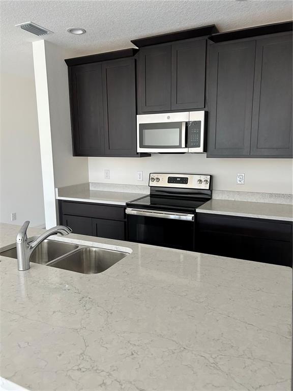A kitchen features dark cabinets, white quartz countertops, and stainless steel appliances — 5002 GREENBANK LANE, KISSIMMEE, FL