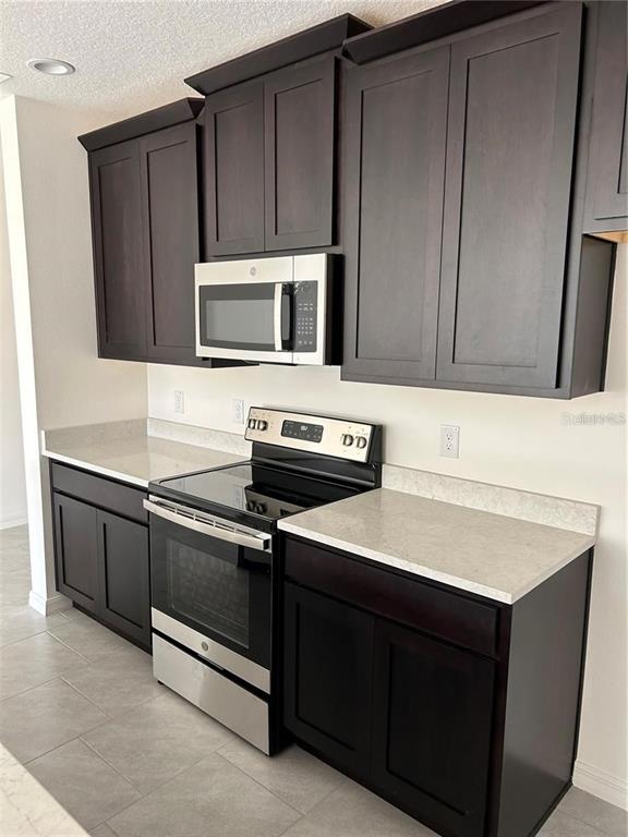 A kitchen features dark wood cabinets, stainless steel appliances, and light-colored countertops — 5002 GREENBANK LANE, KISSIMMEE, FL