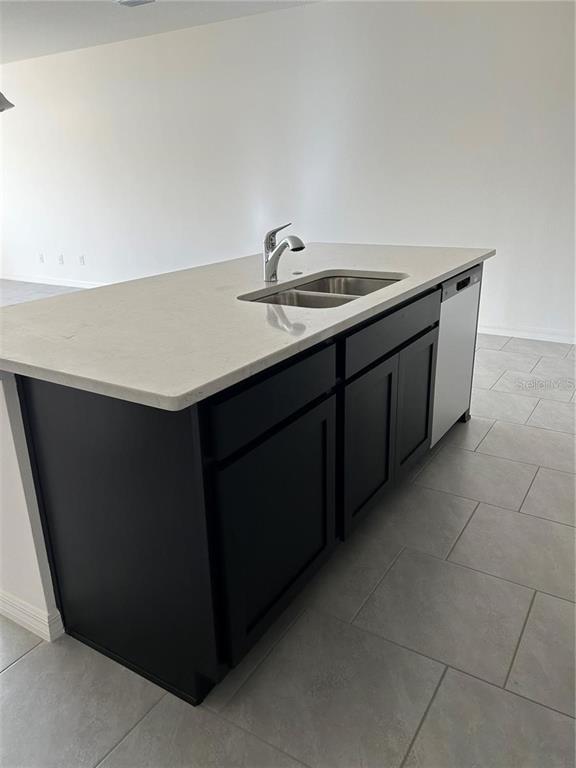 A kitchen island features a stainless steel sink, light countertops, and dark cabinetry — 5002 GREENBANK LANE, KISSIMMEE, FL
