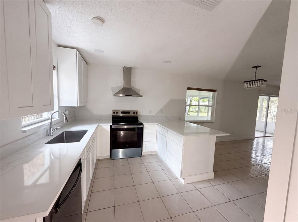 A modern kitchen features white cabinets, quartz countertops, stainless steel appliances, and tiled flooring — 2401 MYAKKA DRIVE, ORLANDO, FL
