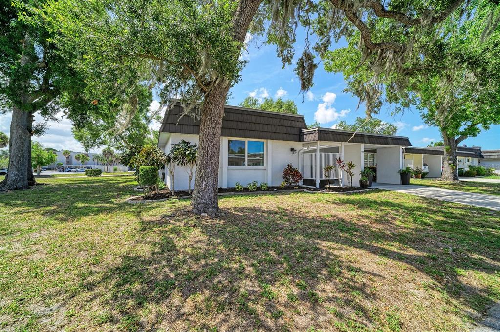 A single-story white house with a dark mansard roof sits under large oak trees — 1520 LAKESIDE WAY UNIT 147, SARASOTA, FL