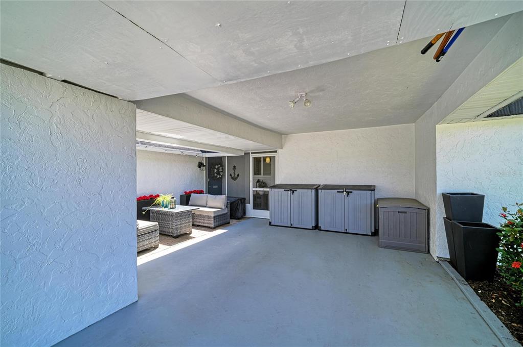 A covered patio features gray concrete flooring, white stucco walls, and several outdoor storage bins — 1520 LAKESIDE WAY UNIT 147, SARASOTA, FL