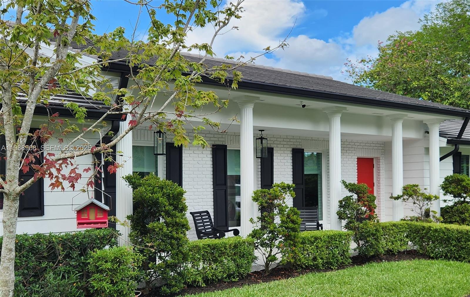 A white brick house exterior features a covered porch with columns and a red door — 10705 SW 128th Ter, Miami FL 33176, MIAMI, FL