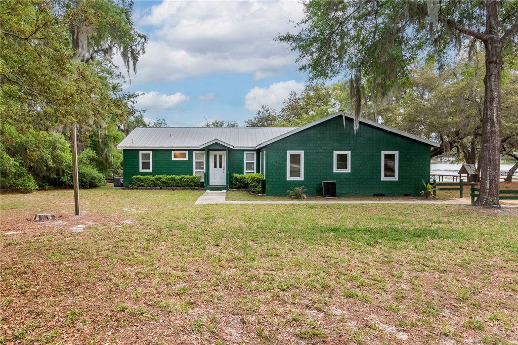 A green, single-story house with a metal roof sits on a grassy lot with trees — 22649 NE 105TH AVENUE ROAD, FORT MC COY, FL