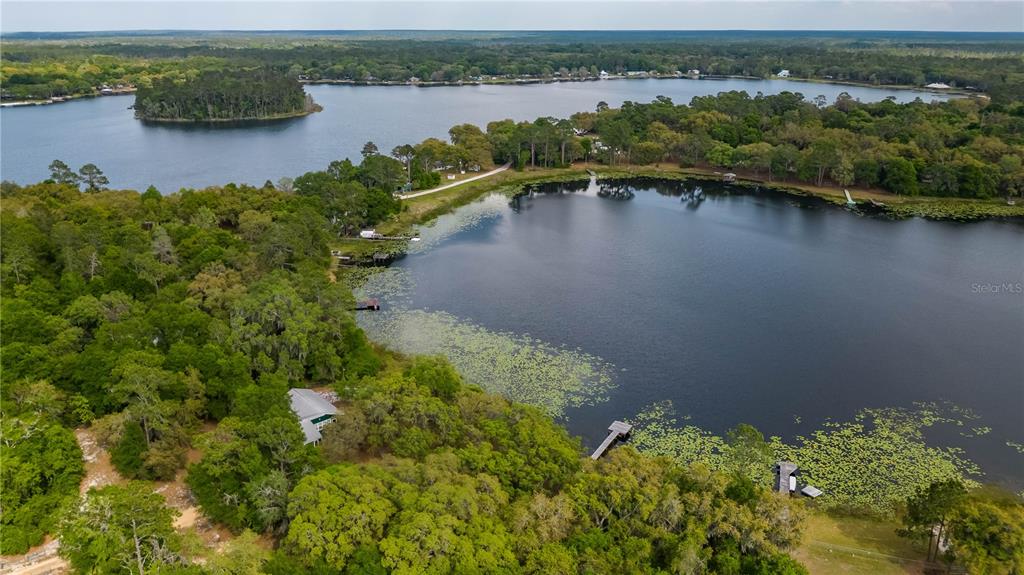 An aerial view shows a house nestled in a wooded area beside a large lake — 22649 NE 105TH AVENUE ROAD, FORT MC COY, FL
