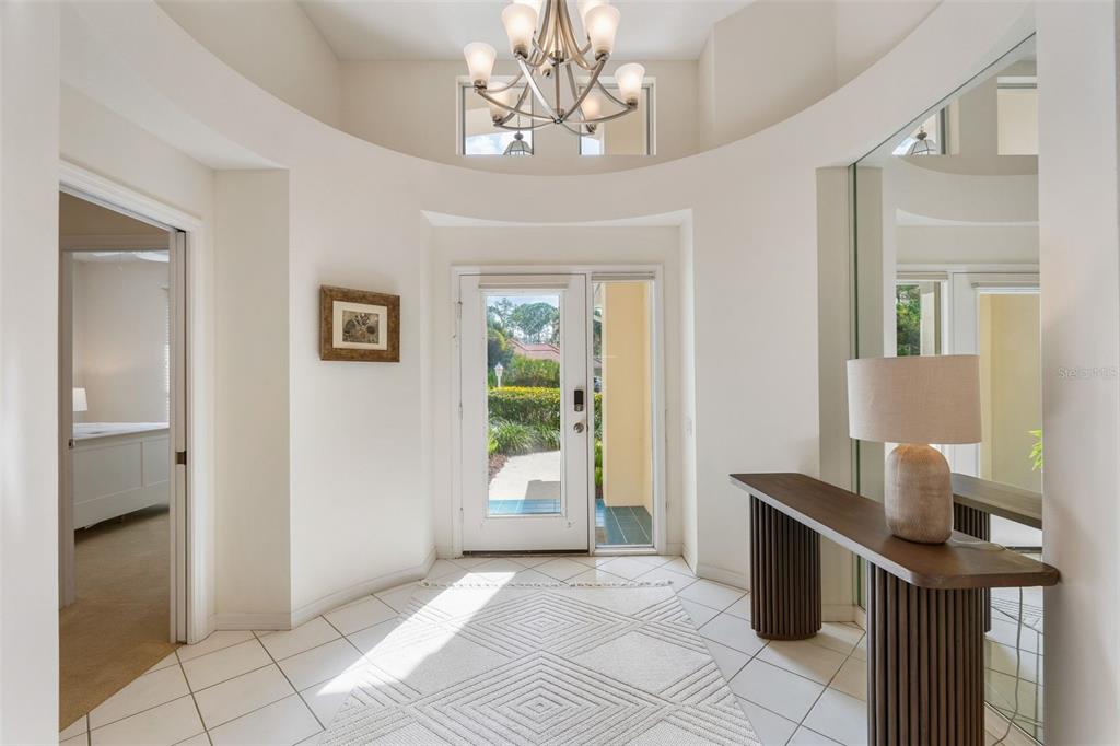 A bright entryway features a tiled floor, a modern chandelier, and a console table — 6427 BERKSHIRE PLACE, UNIVERSITY PARK, FL