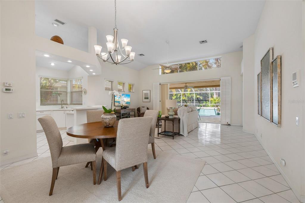 A dining area with a round table and chairs opens into a living room with pool views — 6427 BERKSHIRE PLACE, UNIVERSITY PARK, FL