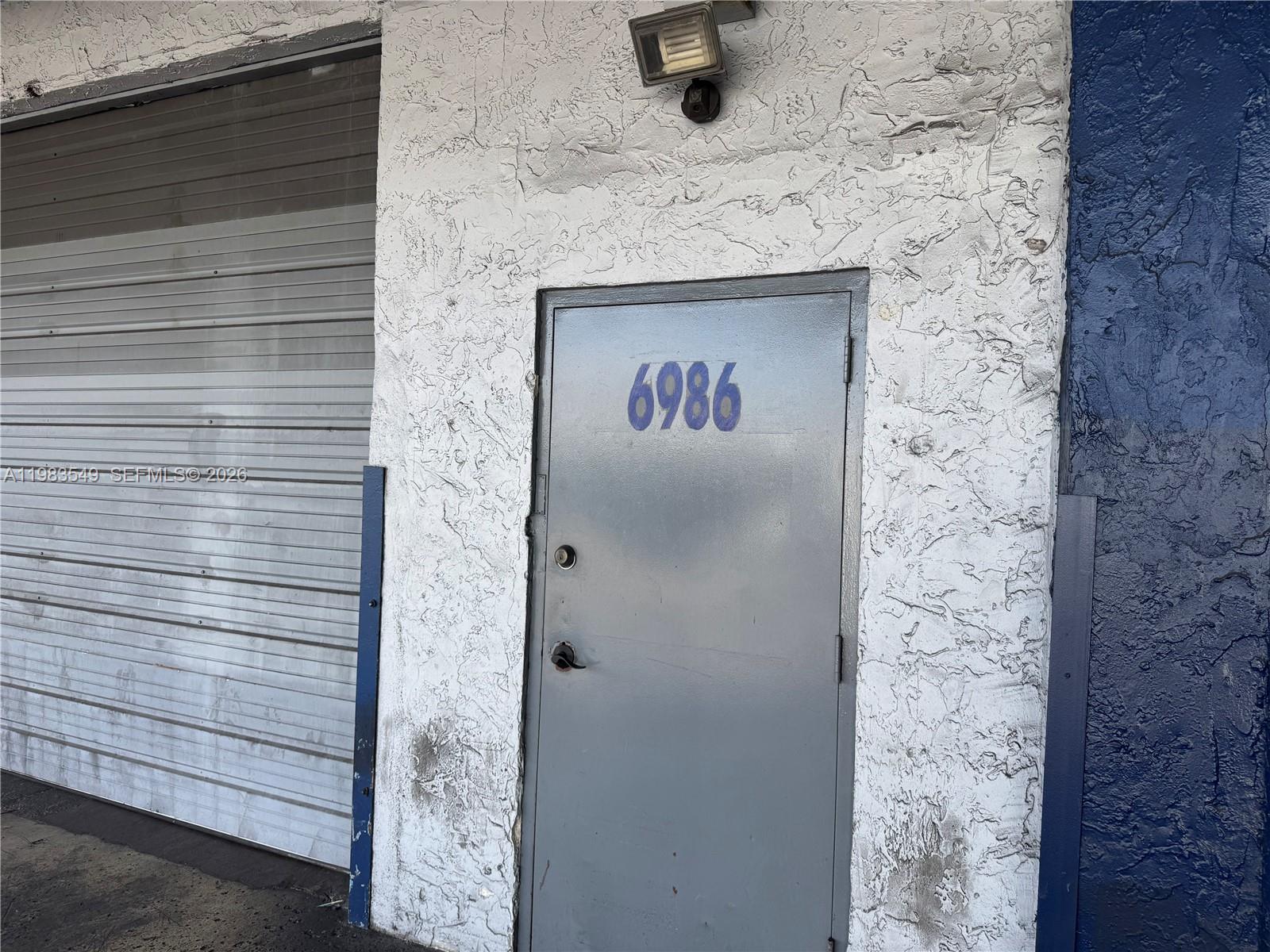 A grey metal door with the number 6986 is set into a textured white wall — 7172 NW 12th St # 6986, Miami FL 33126, MIAMI, FL