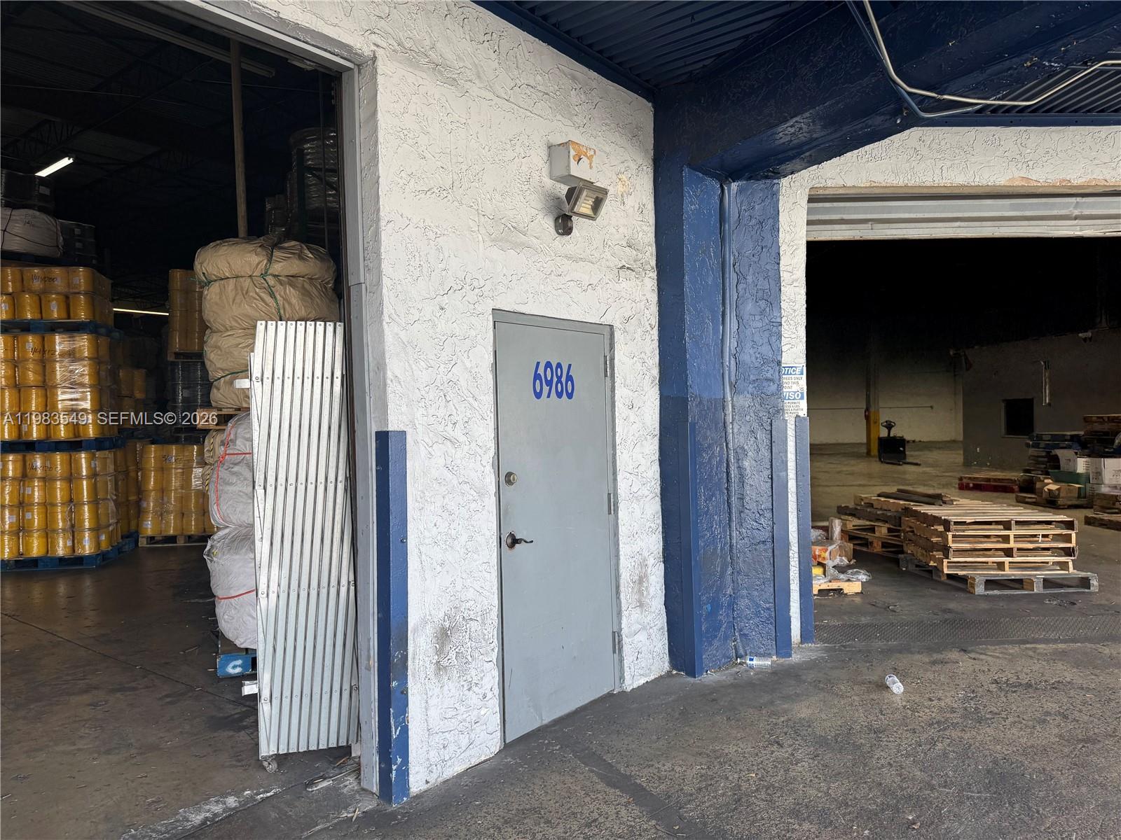 A gray door labeled 6986 sits between two warehouse loading bays with concrete walls — 7172 NW 12th St # 6986, Miami FL 33126, MIAMI, FL