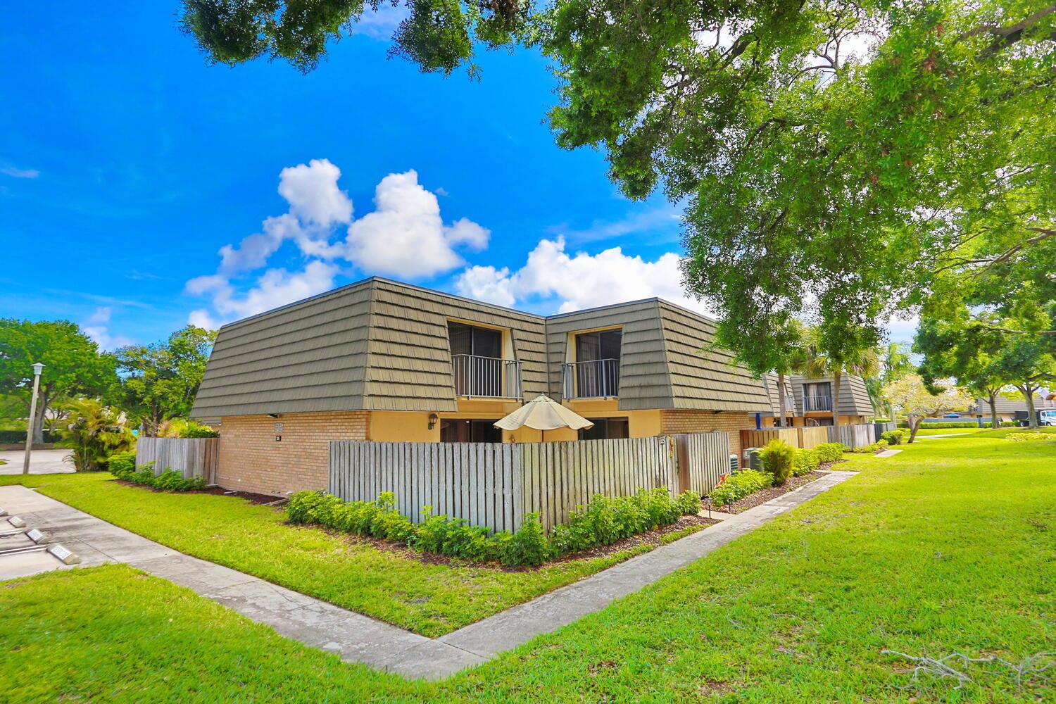 A two-story tan building with a mansard roof and fenced-in patios sits on a lawn — 325 3rd Way, West Palm Beach FL 33407, WEST PALM BEACH, FL