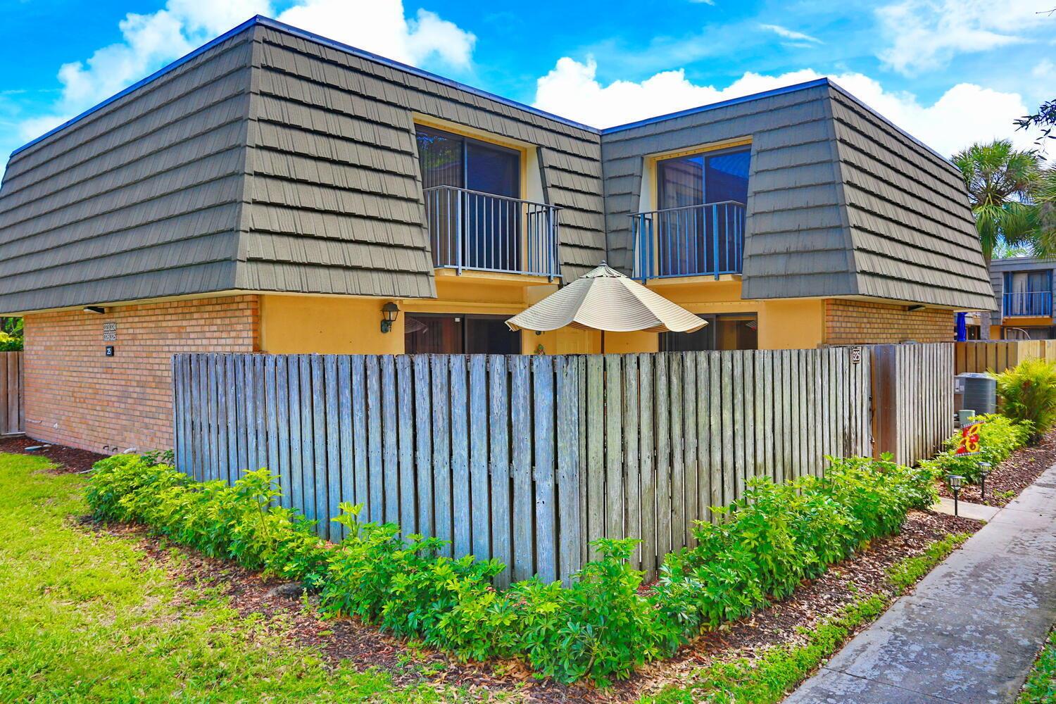 A two-story townhouse with a mansard roof, brick siding, and a fenced-in patio area — 325 3rd Way, West Palm Beach FL 33407, WEST PALM BEACH, FL