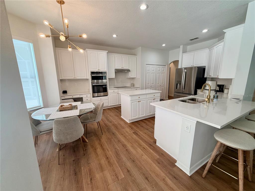A kitchen features white cabinetry, a central island, stainless steel appliances, and wood-look flooring — 167 WESTMORELAND CIRCLE, KISSIMMEE, FL