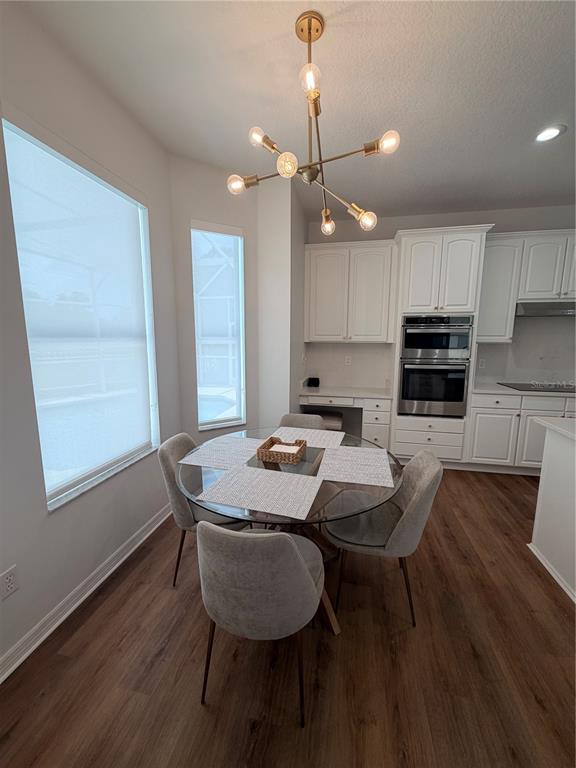 A dining area features a glass table, modern chandelier, and white cabinetry in the kitchen — 167 WESTMORELAND CIRCLE, KISSIMMEE, FL