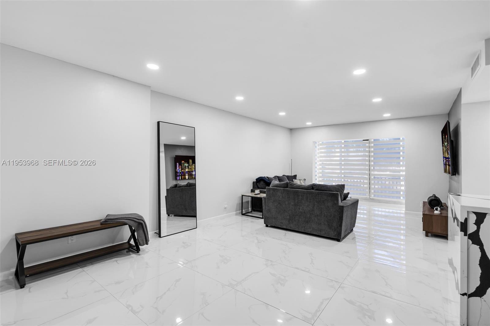 A living room features white marble-look tile floors, a grey sofa, and a floor mirror — 3800 Hillcrest Dr # 203, Hollywood FL 33021, HOLLYWOOD, FL