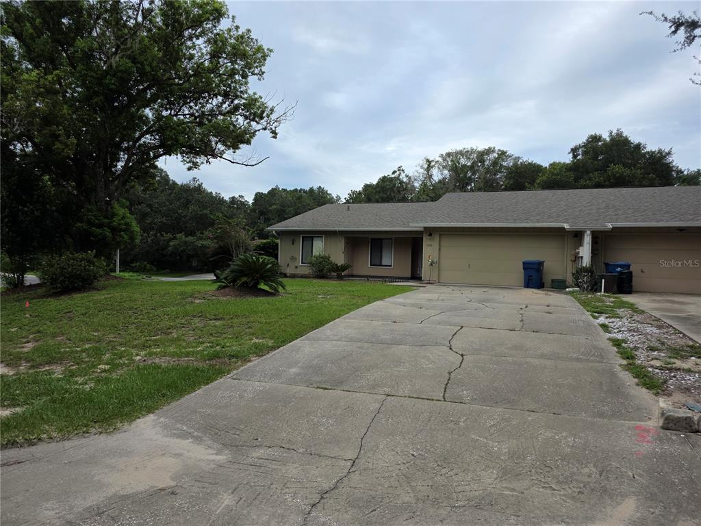 A single-story house with a beige exterior, a two-car garage, and a cracked concrete driveway — 1040 W VILLAGE GREEN ROAD, DELAND, FL