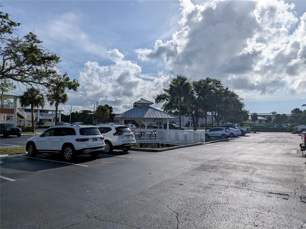 A parking lot features a white gazebo surrounded by palm trees and parked vehicles — 1120 PINELLAS BAYWAY S UNIT 211, ST PETERSBURG, FL