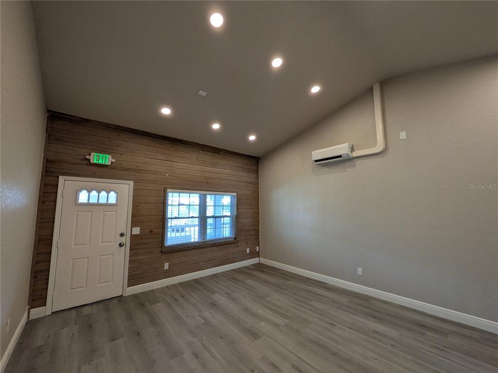 A room with wood-paneled walls, a white door, a window, and a wall-mounted air conditioner — 1120 PINELLAS BAYWAY S UNIT 211, ST PETERSBURG, FL