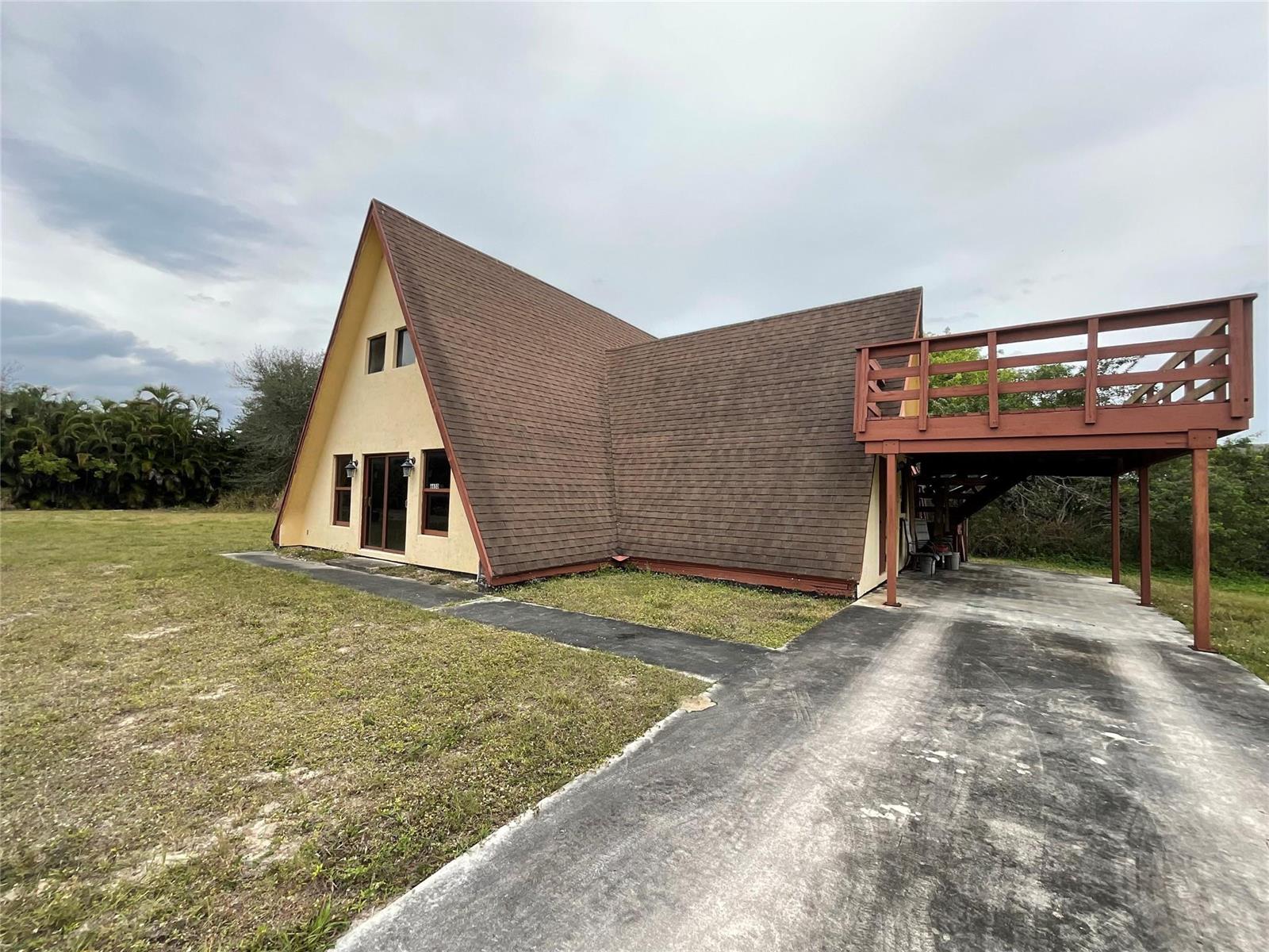 An A-frame house features a brown shingled roof, a raised wooden deck, and a concrete driveway — 6650 Riggers Road, Lake Worth FL 33462, LAKE WORTH, FL